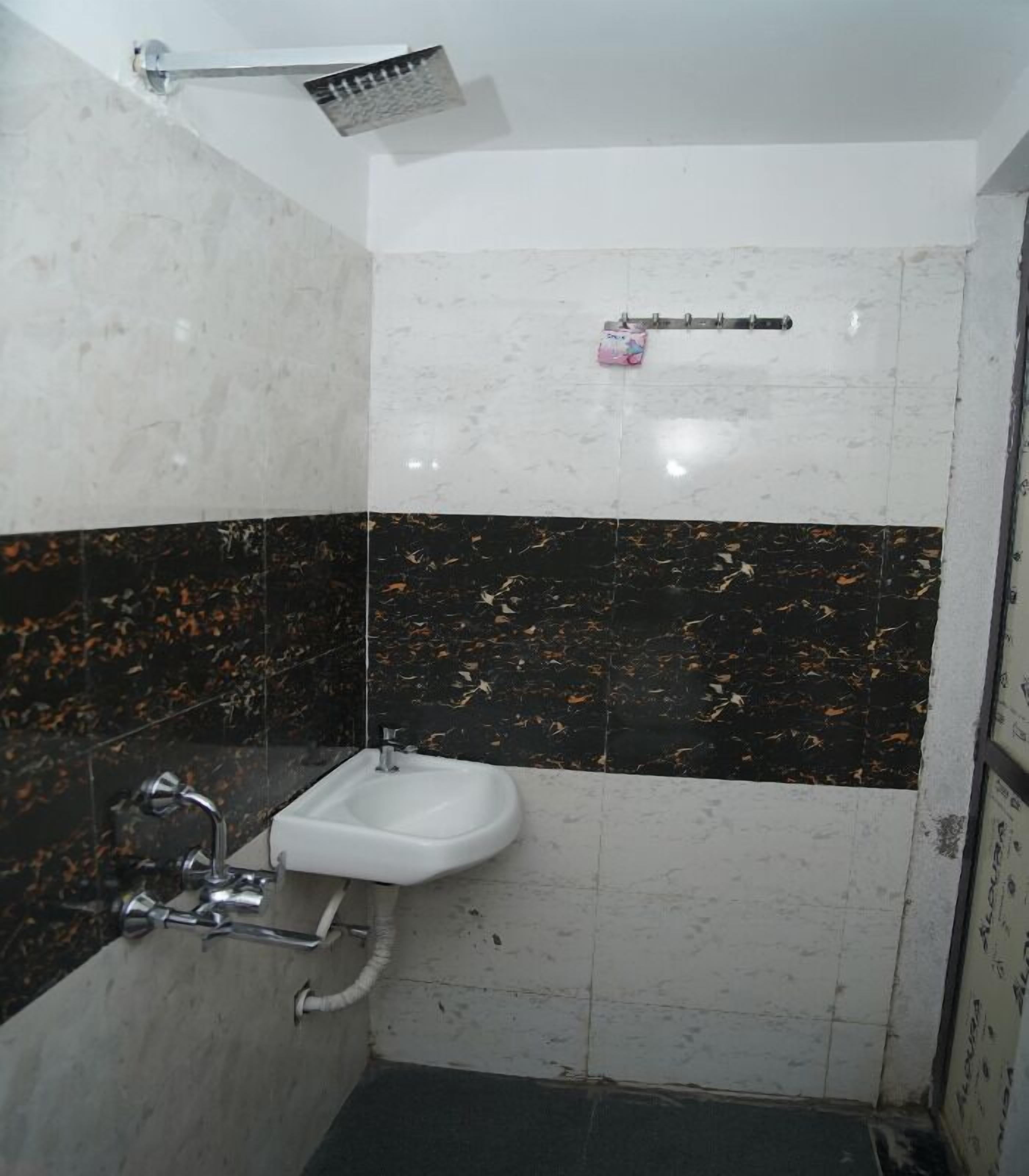 A bathroom with a white sink, a shower, and a black and white tiled wall.