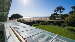 A view from a window with a glass roof overlooking a beach, a grassy area, and a few trees.