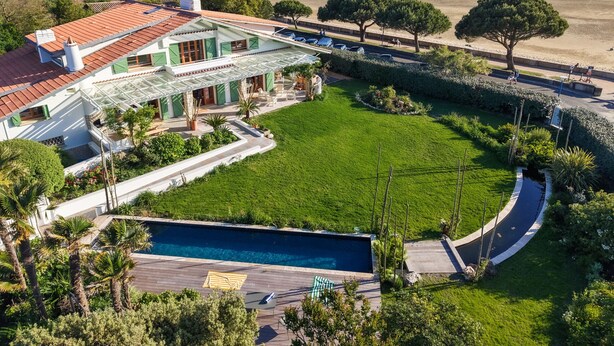 A large house with a swimming pool, green lawn, and a view of the beach.