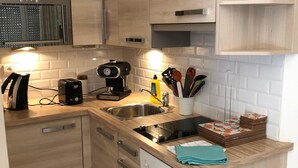 A modern kitchen with wooden cabinets, a built-in oven, a sink, and a small shelf with a decorative item. - Ekin Ô reV (Montauroux)