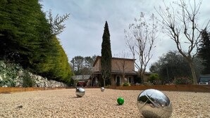 A courtyard with a gravel surface, a tall tree, and a building in the background. - Ekin Ô reV (Montauroux)