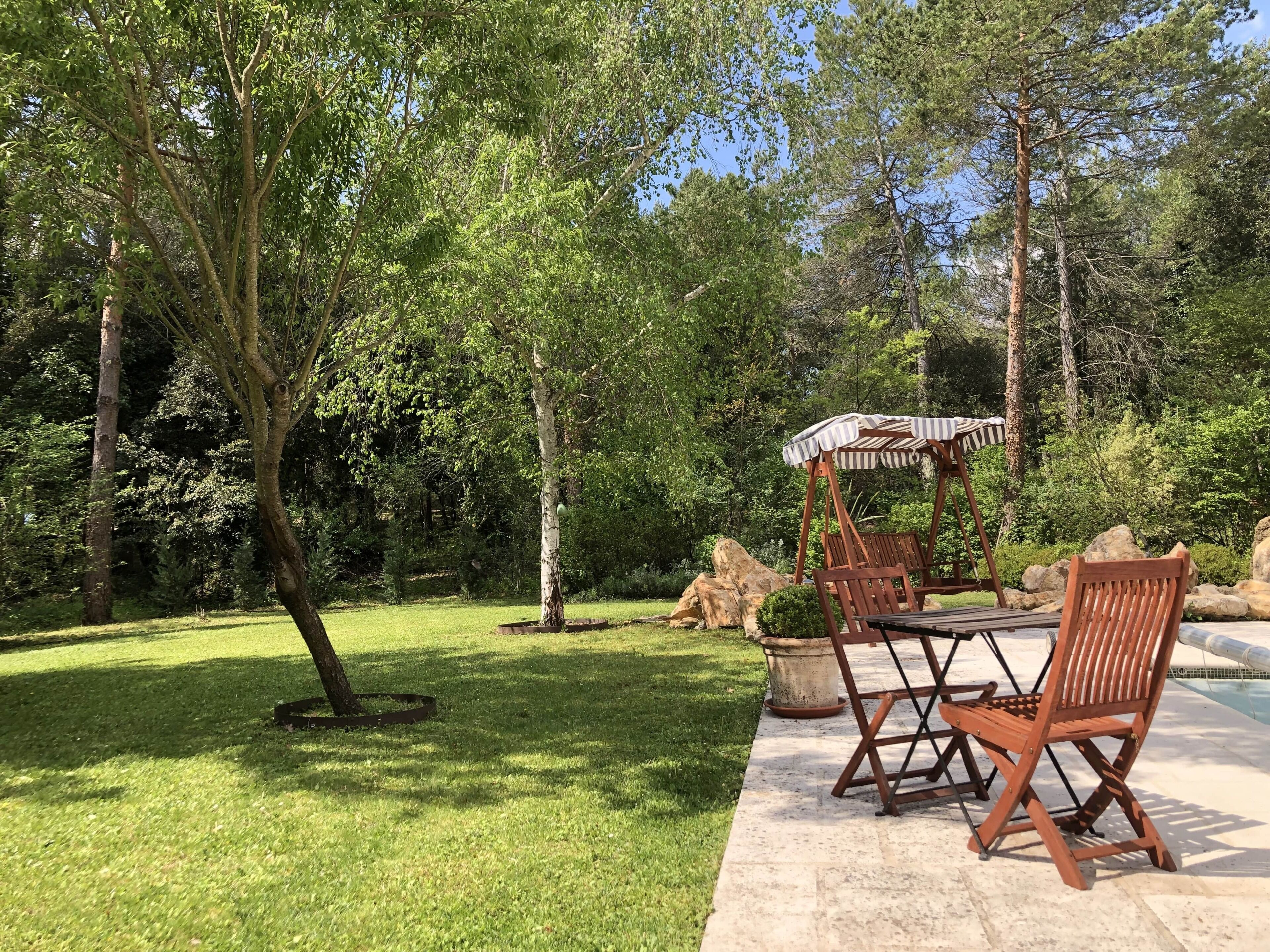 Un patio con mesa y sillas de madera, y un toldo a rayas.