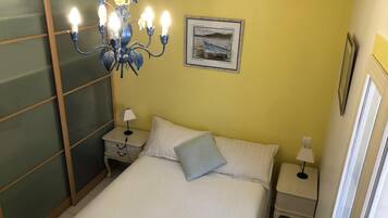 Un dormitorio con cama, mesitas de noche, candelabro, un cuadro en la pared y ventana.