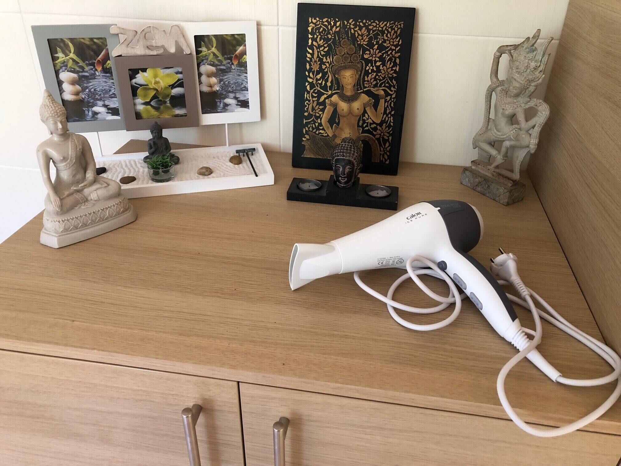 A wooden dresser with a hairdryer, a Buddha statue, framed photos, and decorative items.