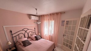A bedroom with a bed, bedside tables, a hanging light fixture, a window with curtains, and a door with glass panels. - Ekin Ô reV (Montauroux)