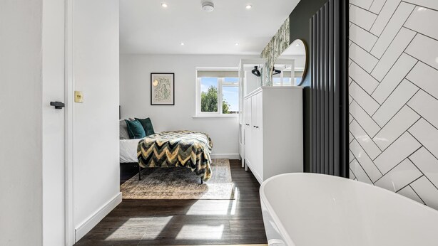 A modern bedroom with a bed, a window, a radiator, and a bathroom with a bathtub.