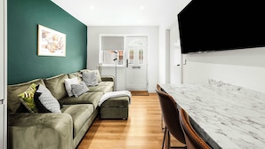 A modern living room with a green wall, a sofa, a dining table with chairs, and a door leading to another room.