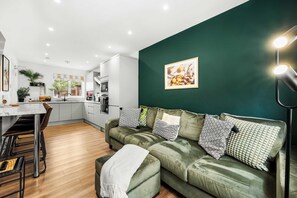Un salon moderne avec un canapé vert, un coin repas et une cuisine en arrière-plan.