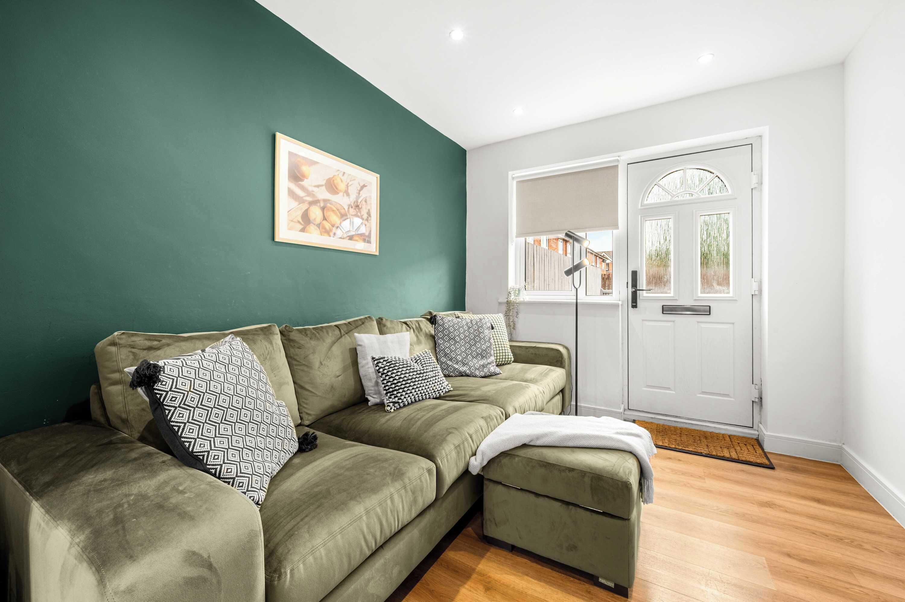 A green sofa with patterned cushions, a framed picture on the wall, and a white door with a window.