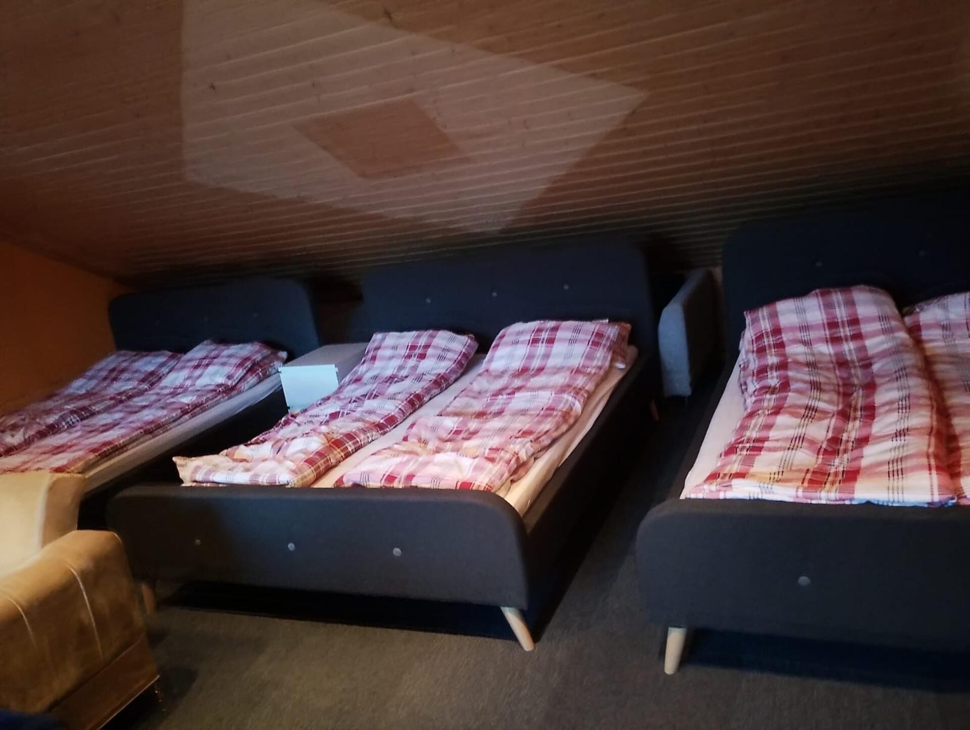 A room with three beds, each with a dark headboard and a red and white checkered blanket.