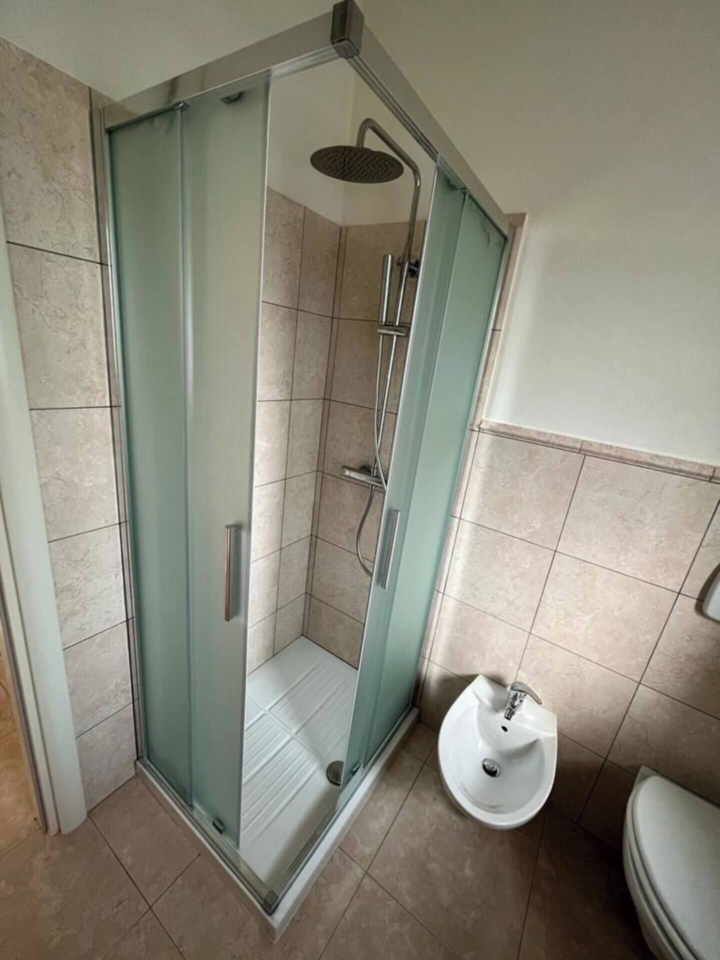 Une douche à l’italienne avec des parois en verre, un pommeau de douche amovible, un lavabo indépendant et des toilettes.