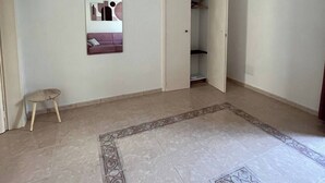 Ein geräumiger Raum mit Fliesenboden, einer Pendelleuchte, einem Kleiderständer und einer Tür zu einem Schrank.