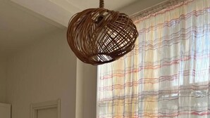 Ein Zimmer mit einem weißen Tisch, einer hängenden Lampenschirm aus Weidengeflecht und einem Fenster mit gestreiften Vorhängen.