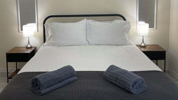 A neatly made bed with white linens, two bedside tables with lamps, and a large mirror on the wall. - Texas Music City is a 5-minute walk from this 2 bedroom apartment (Lindale)
