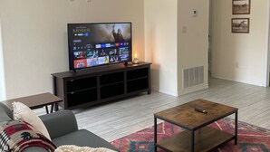 A living room with a gray sofa, a coffee table, a TV on a stand, a ceiling fan, and a patterned rug. - Texas Music City is a 5-minute walk from this 2 bedroom apartment (Lindale)