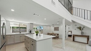 A spacious kitchen with a central island, a dining area with a table and chairs, a staircase leading to an upper level, and a living room with a sofa and a console table. - Modern 3BR Home w/ Backyard in South Austin (Austin)