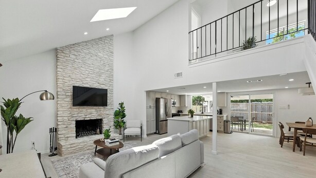 A spacious living room with a stone fireplace, a grey sofa, and a dining area with a table and chairs. - Modern 3BR Home w/ Backyard in South Austin (Austin)
