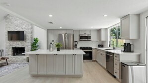 A modern kitchen with a central island, stainless steel appliances, and a stone fireplace. - Modern 3BR Home w/ Backyard in South Austin (Austin)