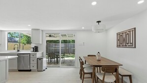 A modern kitchen with white cabinetry, a dishwasher, and a dining area with a wooden table and chairs. - Modern 3BR Home w/ Backyard in South Austin (Austin)