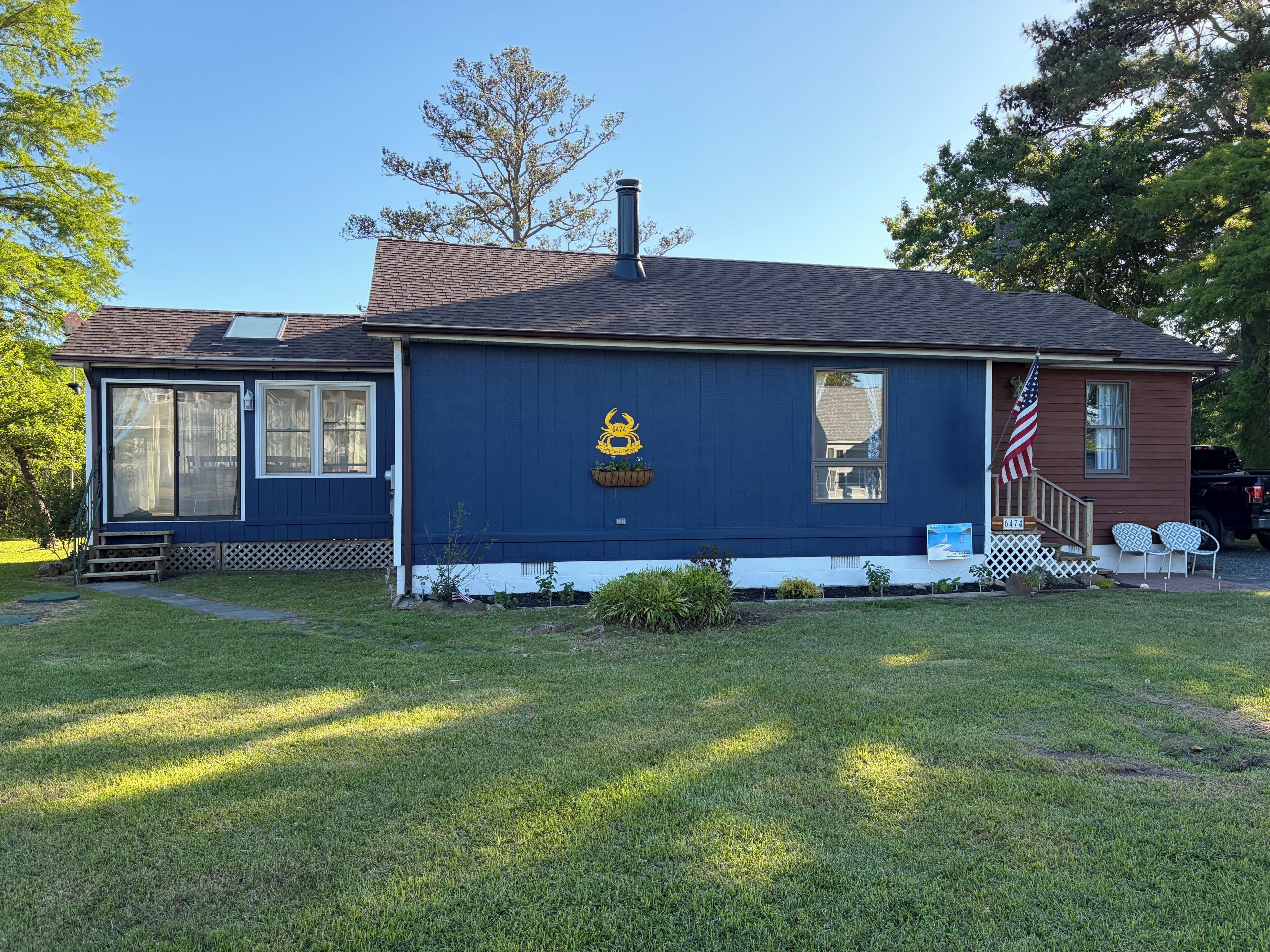 A single-story house with a dark blue exterior, a chimney, a front porch with a small American flag, and a mailbox.