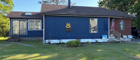 A single-story house with a dark blue exterior, a chimney, a front porch with a small American flag, and a mailbox.
