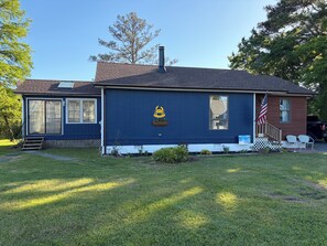 Ein eingeschossiges Haus mit dunkelblauer Fassade, einem Schornstein, einer Veranda mit einer kleinen amerikanischen Flagge und einem Briefkasten.