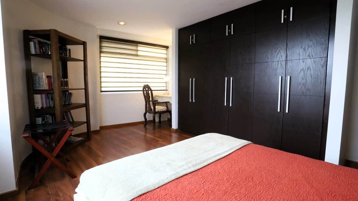 A bedroom with a bed, a bookshelf, a desk, and a wardrobe.