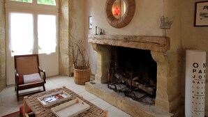 A room with a stone fireplace, a wooden chair, a wicker basket, and a framed mirror on the wall.