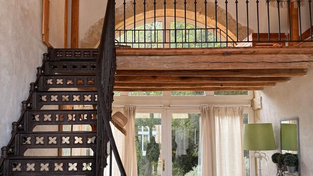 A rustic interior with a wooden staircase, a rocking chair, and a dining area with a table and chairs.