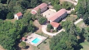 An aerial view of a rural property with multiple buildings, a swimming pool, and surrounding greenery.