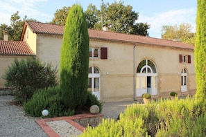 A two-story building with a tiled roof, arched windows, and a gravel driveway.