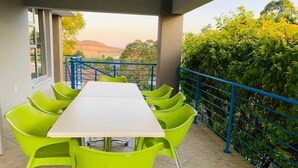 Un espace extérieur abrité, aménagé pour les repas, avec une table blanche et des chaises vert vif, offrant une vue sur un paysage pittoresque.