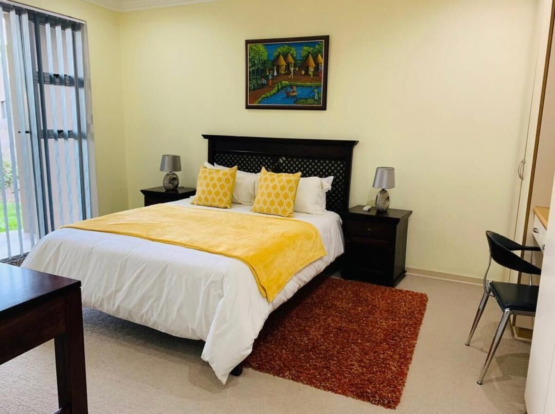 Quarto com cama, duas mesas de cabeceira, escrivaninha, cadeira e um quadro na parede.
