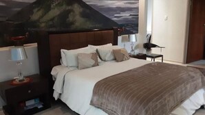 Un lit bien fait, recouvert d’une couverture marron, une table de chevet avec une lampe et un tableau accroché au mur.