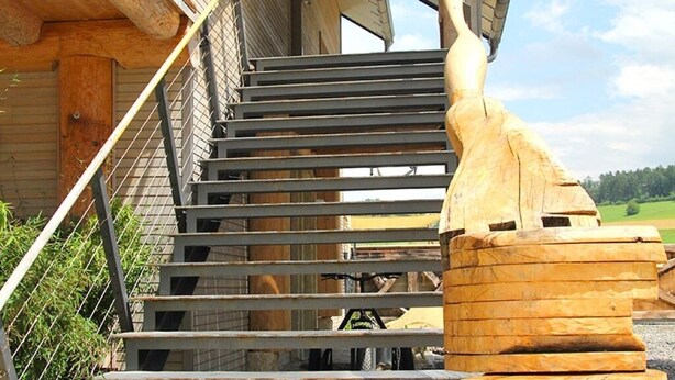 Een houten trap die leidt naar een overdekte veranda met uitzicht op een groen landschap.