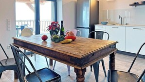 Een eettafel met stoelen, een keuken met een koelkast, en een raam met uitzicht.