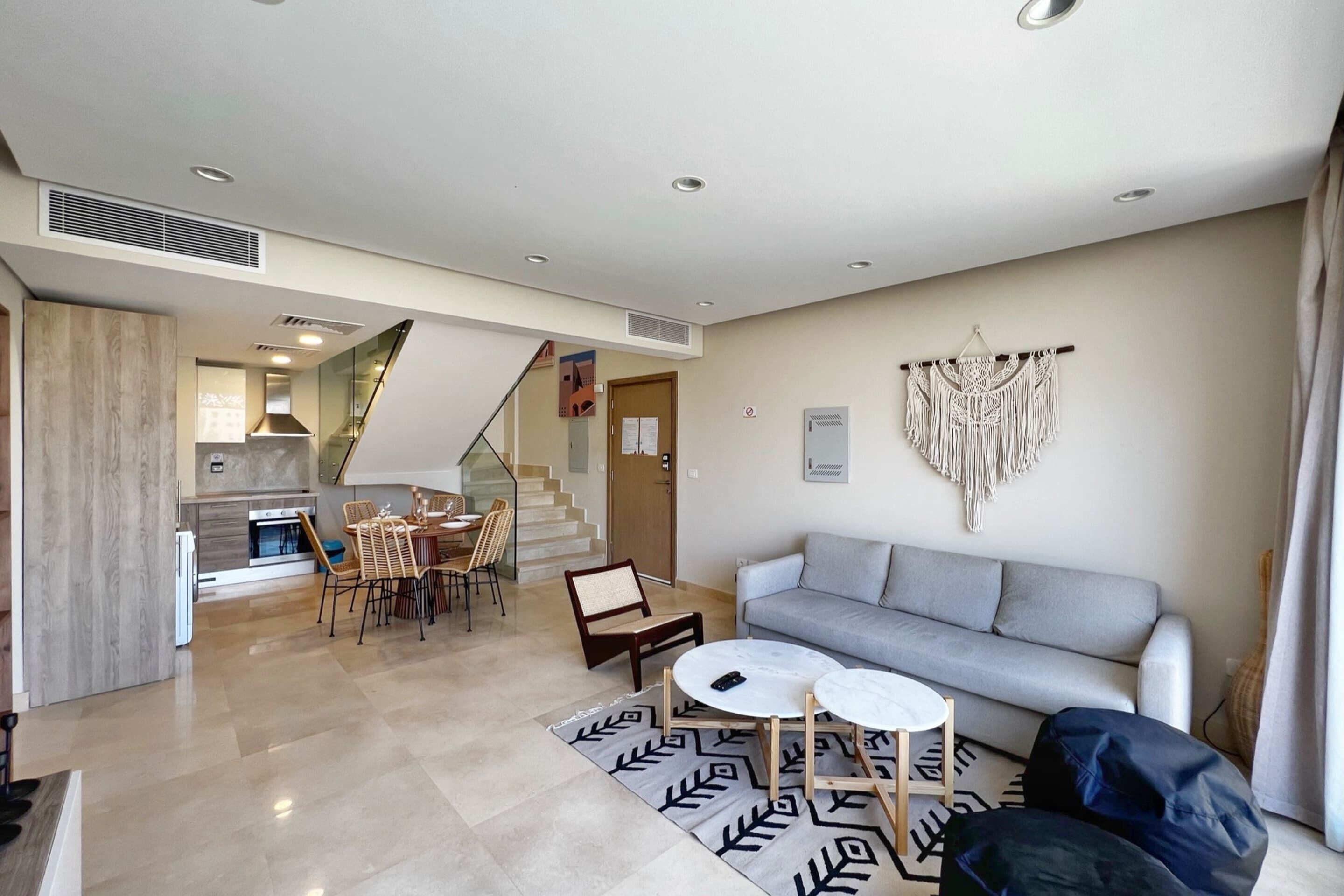 A modern living room with a grey sofa, a coffee table, and a dining area with chairs and a table.