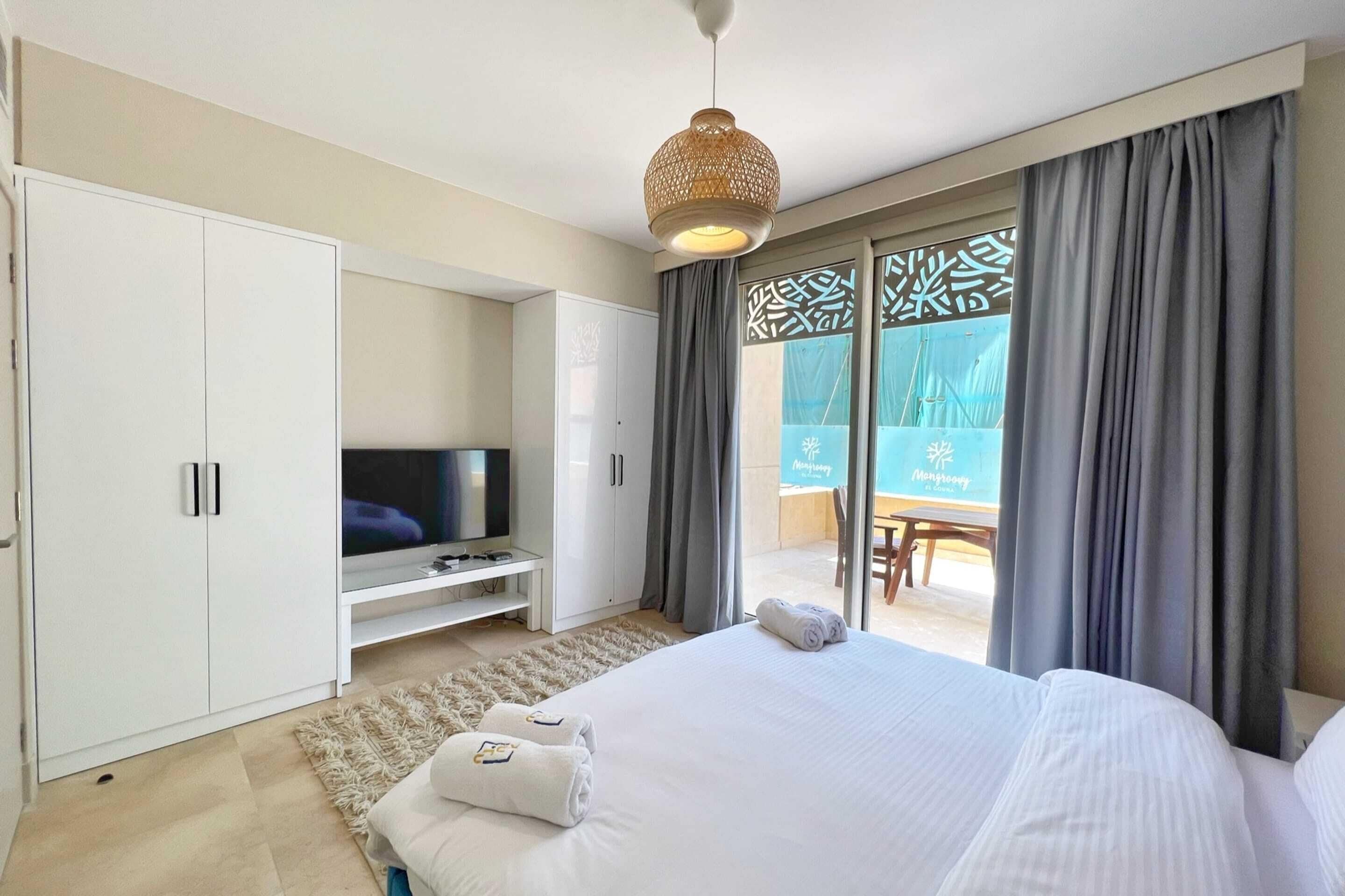 Habitación de hotel con cama, televisor, armario y balcón con vistas.