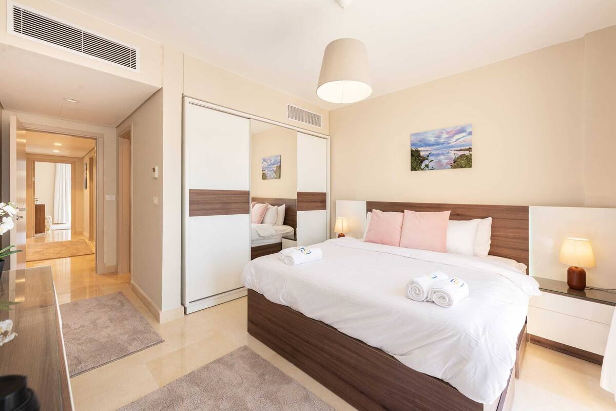 A hotel room with a large bed, a bedside table with a lamp, a mirror, and a painting on the wall.