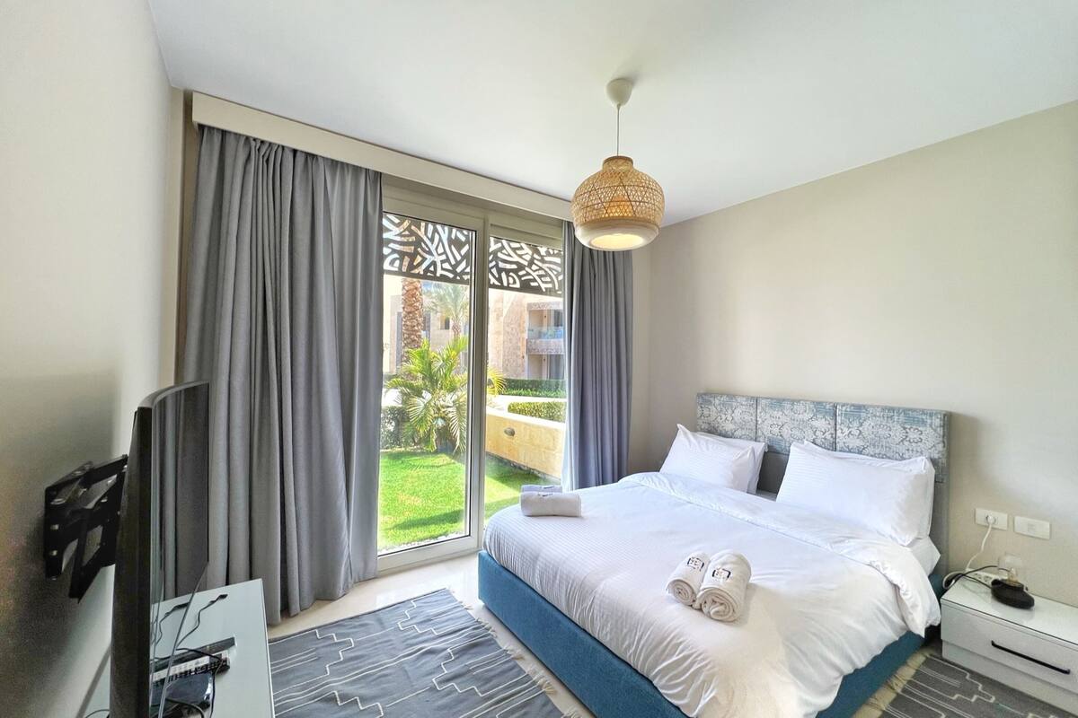 A hotel room with a bed, a TV, a desk, and a view of the outdoors.