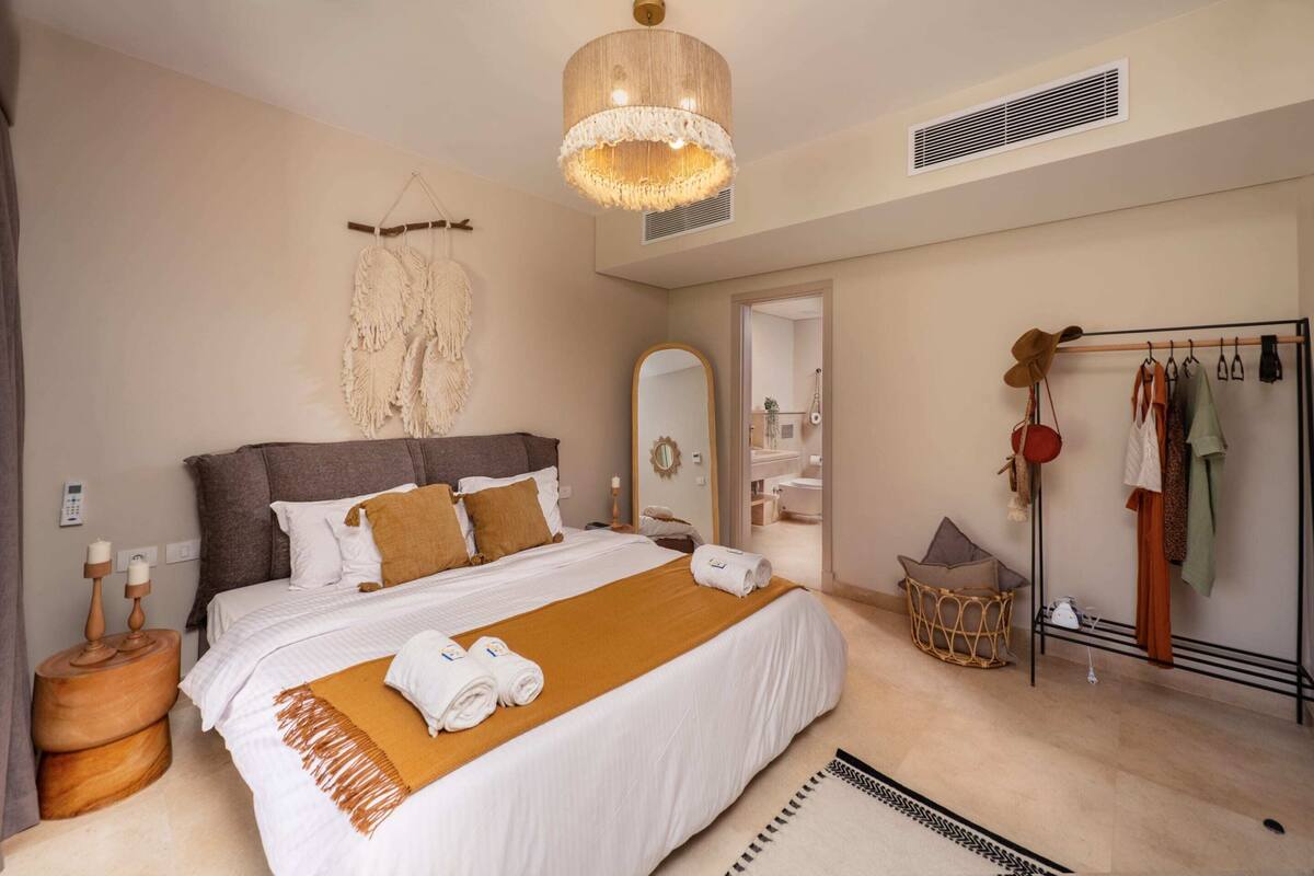 A well-appointed bedroom with a large bed, a hanging macrame piece, a mirror, and a clothing rack.