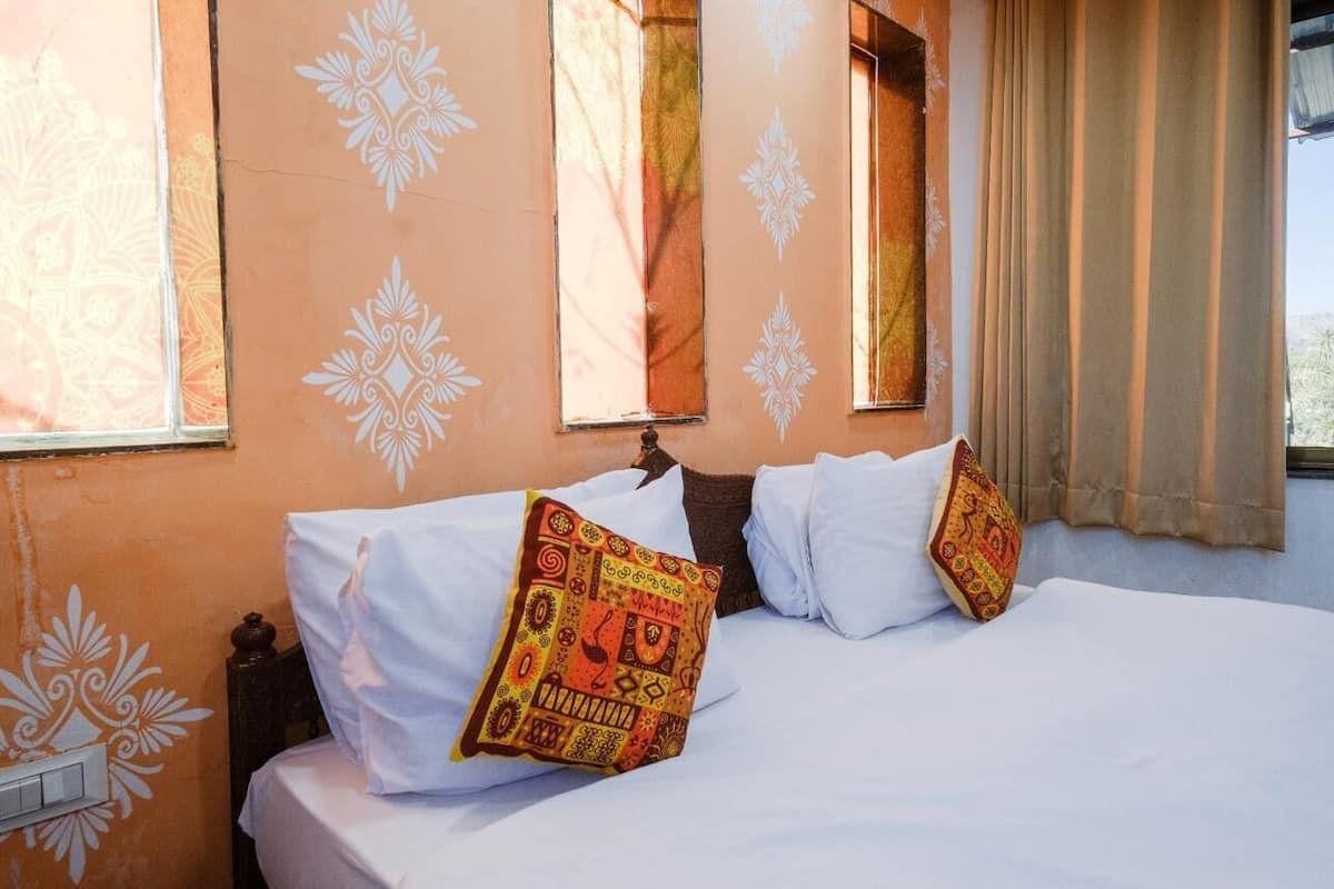 A hotel room with a bed, two pillows, a nightstand, and a window with curtains.