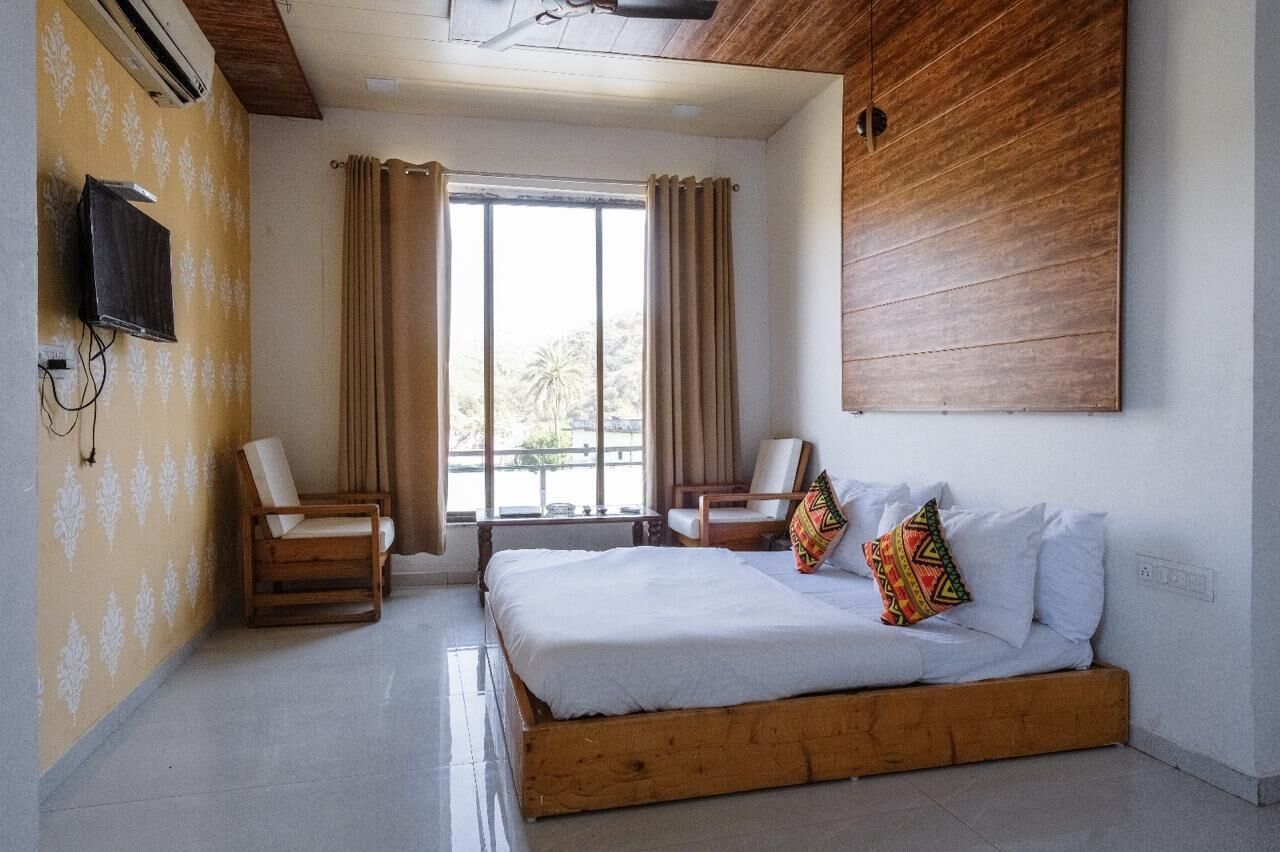 A bedroom with a wooden bed, two chairs, a TV, and a window with curtains.