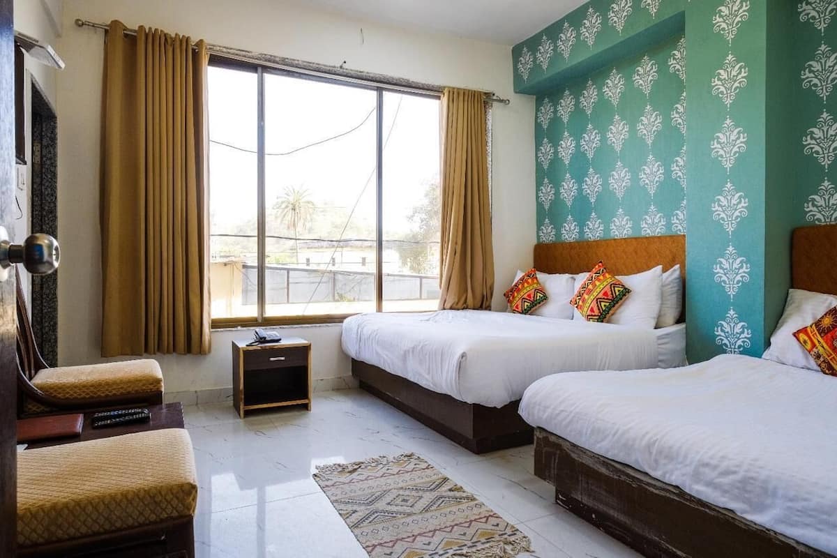 A hotel room with two beds, a small table, a chair, and a window with curtains.