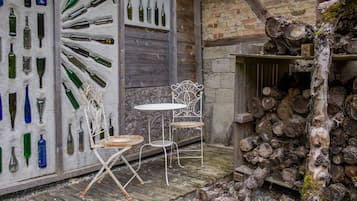 Un área de estar al aire libre con estilo rústico, con sillas de metal y una mesa, rodeada por una terraza de madera y un muro de ladrillo.