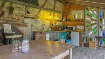Een landelijke keuken met een houten tafel, een schoolbord met een welkomstboodschap, en een muur versierd met lege flessen.