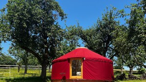 A red yurt with a wooden platform in a grassy area with trees.