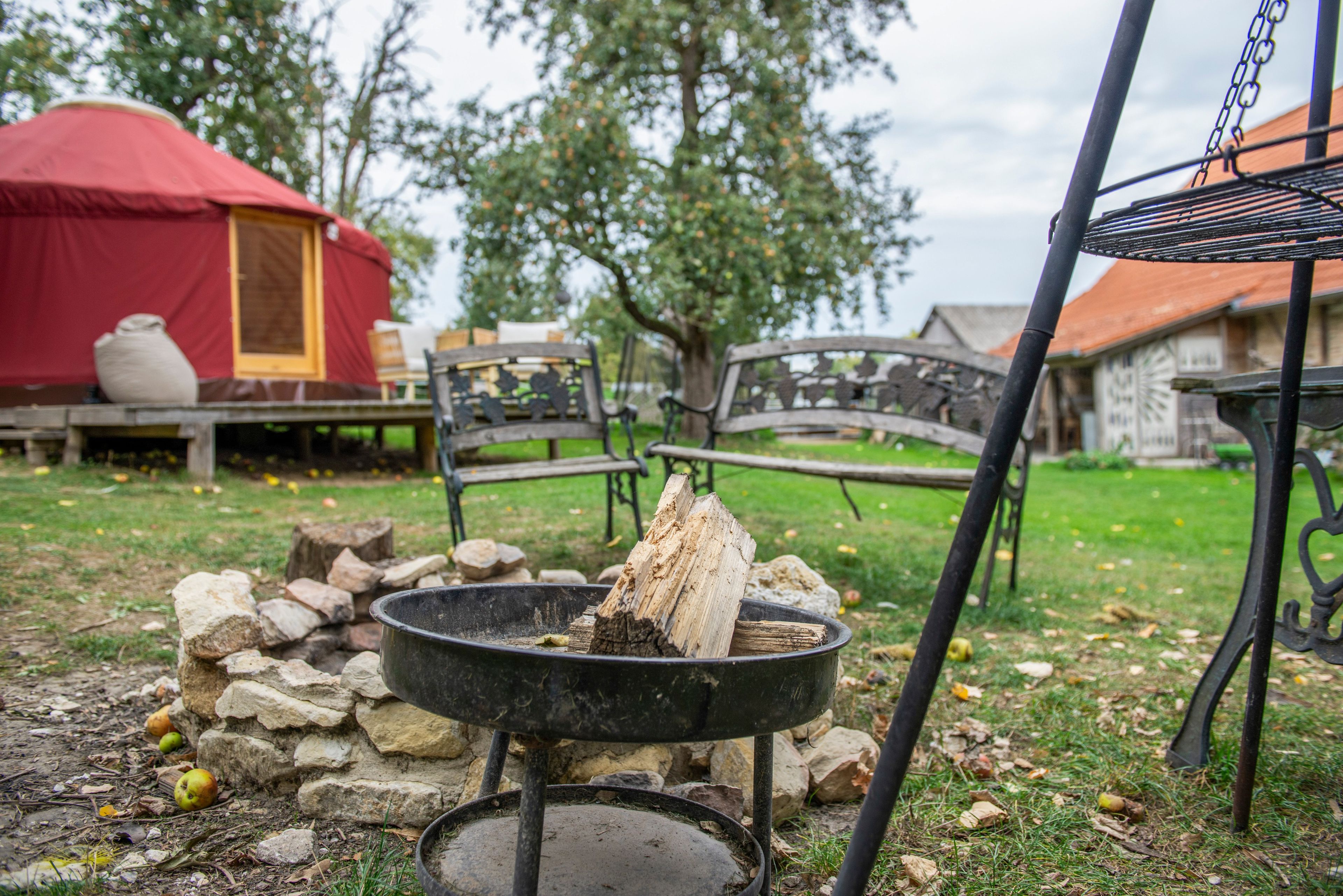 A campsite with a fire pit, a red tent, and a metal bench.
