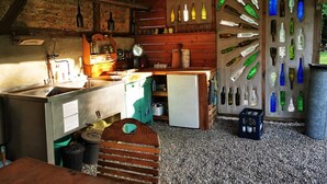 A rustic kitchen with a wooden counter, a chalkboard sign, and a wall of empty bottles.