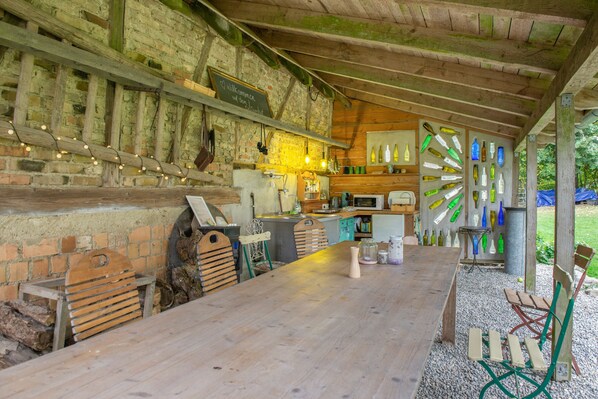 A rustic outdoor dining area with a brick wall, wooden beams, and a variety of seating options including benches and chairs.